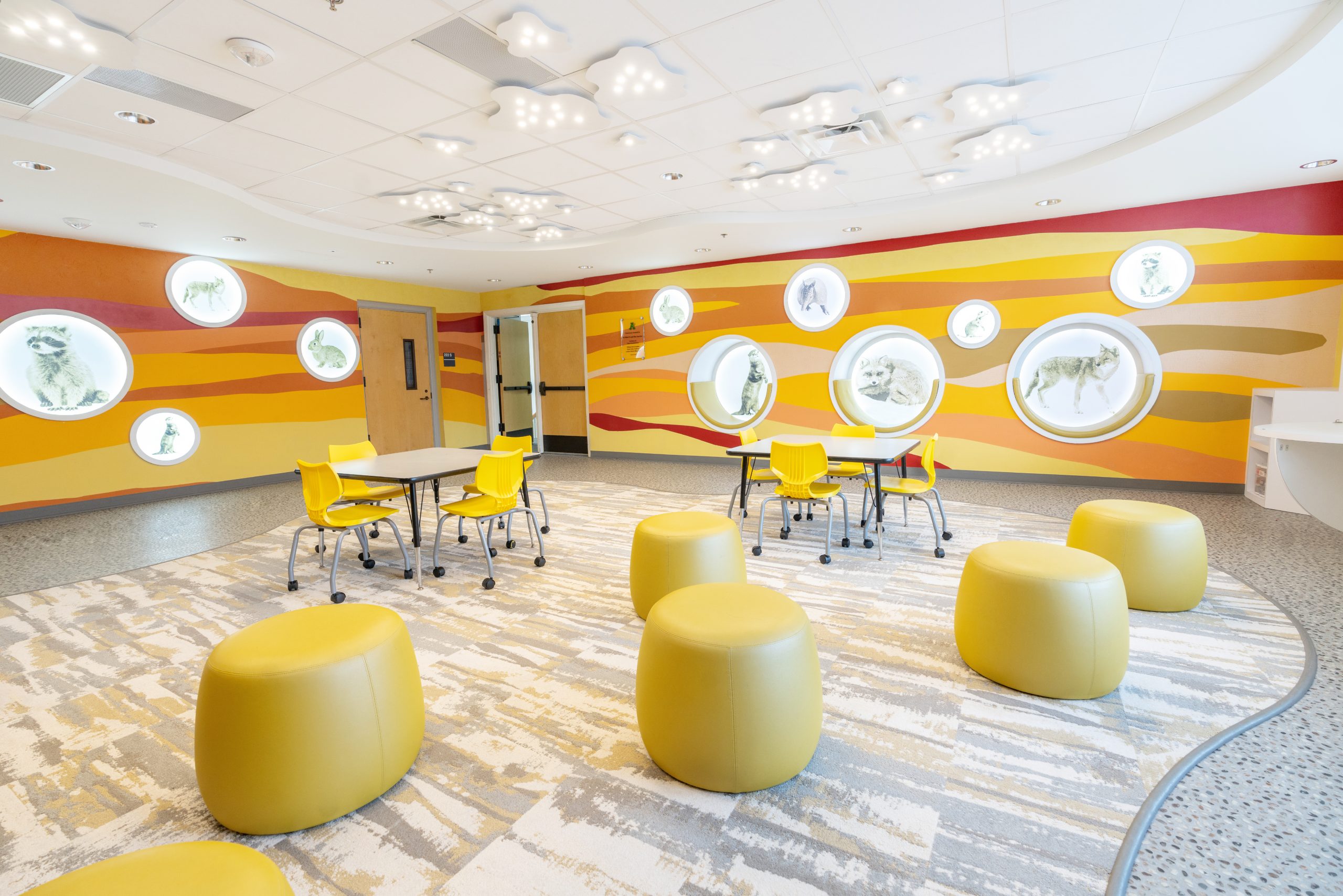 Soil zone learning space with layered wave mural, wildlife porthole wall displays, and cloud-shaped ceiling lights at Armstrong Elementary