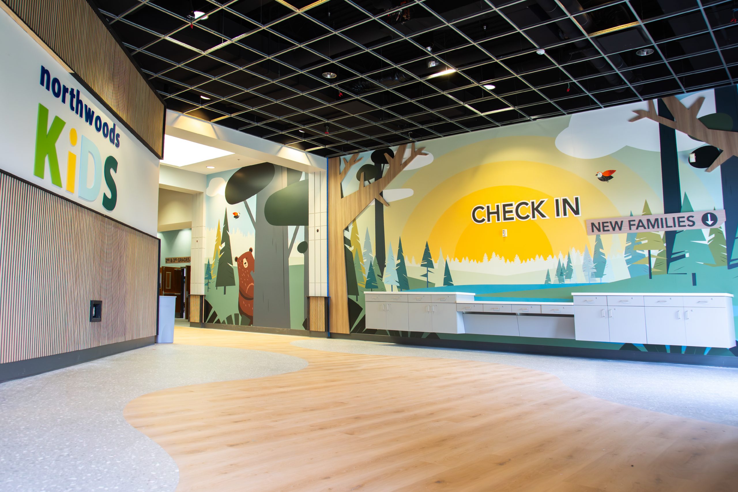 Northwoods Kids branded environment with sunrise forest mural, dimensional signage, and check-in wayfinding by Enviropop