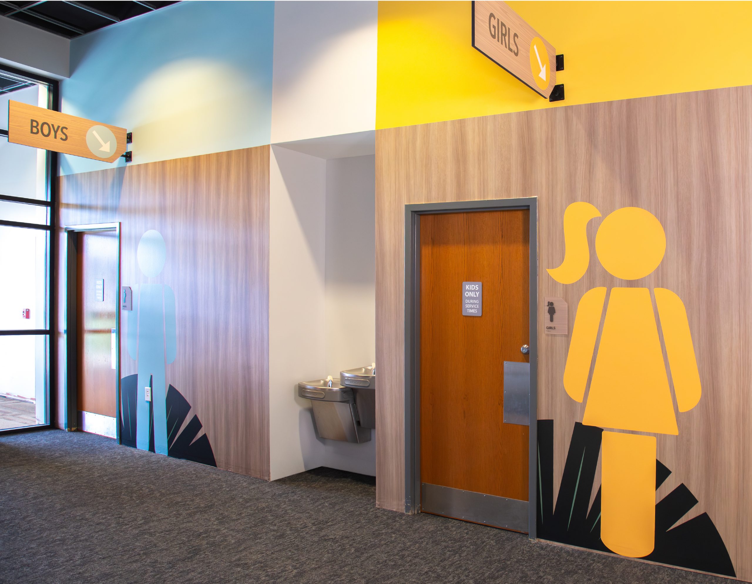 Boys and girls restroom wayfinding signage with wood-grain wall design at Northwoods Kids by Enviropop